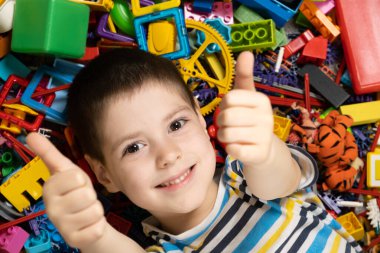 Mutlu 5 yaşındaki çocuk oyuncakların arasında baş parmak gösteriyor..