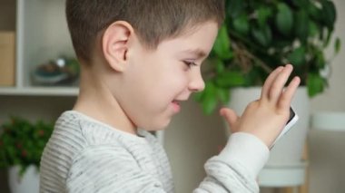 Anaokulundan bir çocuk akıllı telefondan oyun oynuyor parmaklarını ekranda gezdiriyor ve konuşuyor..