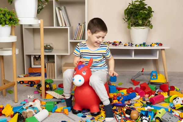 A little 5-year-old boy jumps on an inflatable donkey toy in the childrens room among a mess, scattered toys