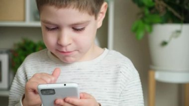 Anaokulundan bir çocuk akıllı telefondan oyun oynuyor parmaklarını ekranda gezdiriyor ve konuşuyor..