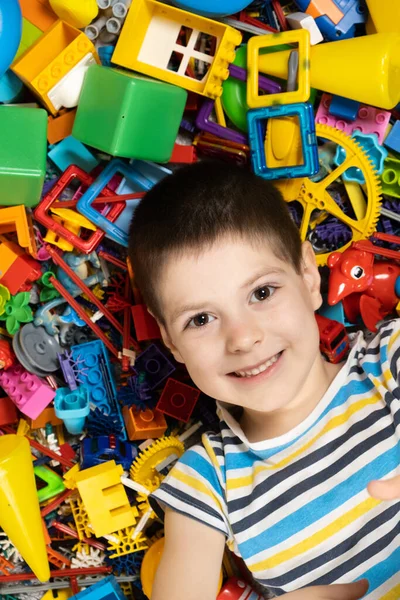 Portrait of a 5-year-old boy against the background of scattered toys. Happy childhood, abundance of toys.