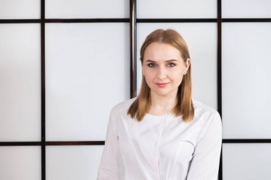 Siyah beyaz arka planda beyaz üniformalı sarışın bir doktorun portresi.