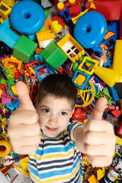 stock image Happy 5 year old boy showing thumbs up lying among toys, top view.