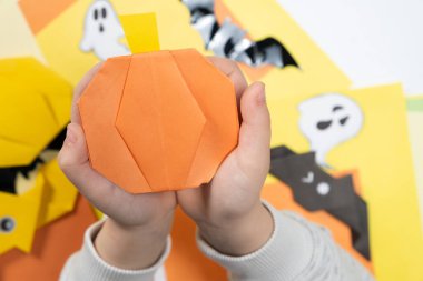 Cadılar Bayramı için Origami el sanatları - bir çocuğun elindeki kağıttan yapılmış balkabağı, üst görünüm