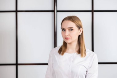 Siyah beyaz arka planda beyaz üniformalı sarışın bir doktorun portresi.