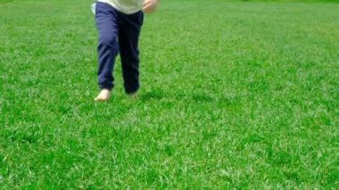 Çıplak ayaklı çocuk çimlerin üzerinden kameraya doğru koşuyor, ağır çekimde. Sağlıklı ve mutlu bir çocukluk