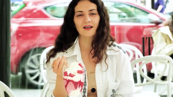 若いブルネットの女性は屋外カフェでガラスボウルからスプーンでアイスクリームを食べる — ストック動画
