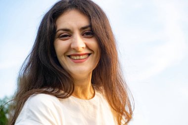 35 yaşında neşeli, esmer bir kadının gökyüzüne bakan portresi. Yazı yazılacak bir yer.