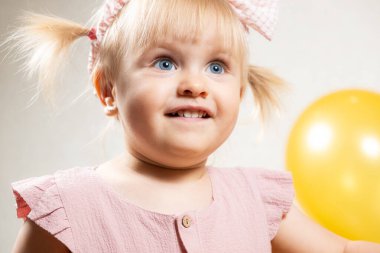 Mavi gözlü ve sarı balonlu iki yaşında sarışın bir kızın portresi..