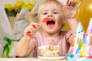 Doğum gününde pasta yiyen iki yaşında sarışın bir kız.