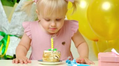 Kafasında iki at kuyruğu olan şirin bir doğum günü kızı doğum günü pastasında bir mum söndürdü.