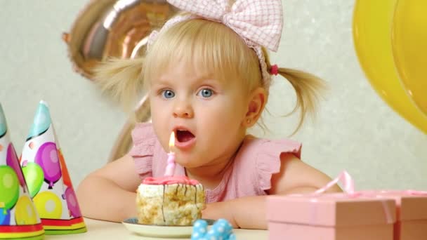 2歳の少女が誕生日ケーキにろうそくを吹き消し願い事をする — ストック動画