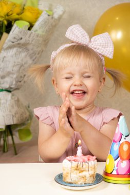 Sevimli küçük kız doğum gününde bir dilek tutuyor, elinde mumla bir pastanın önünde oturuyor.