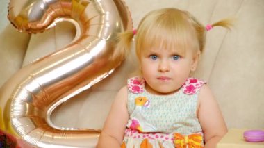 Doğum gününde iki at kuyruklu gülümseyen iki yaşındaki bir kızın portresi..