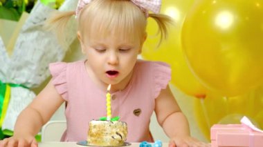 Kafasında iki at kuyruğu olan şirin bir doğum günü kızı doğum günü pastasında bir mum söndürdü.