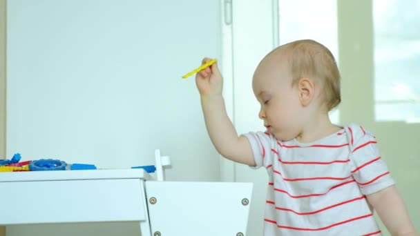 1歳の子供がテーブルから床にデザイナーの部分を投げる — ストック動画