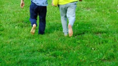 Küçük bir oğlan ve bir kız çimlerin üzerinde yalınayak koşuyorlar. Çocukların arkadaşlığı ve mutlu çocukluk kavramı..