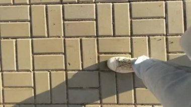 Açık renk kot ve beyaz spor ayakkabılı bir kadın kaldırım levhaları, üst manzara, yakın plan bacaklar, basamaklar üzerinde yürüyor..