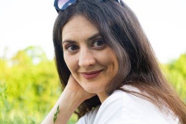 35 yaşında esmer bir kadının portresi. Doğaya gülümseyen kameraya bakıyor.