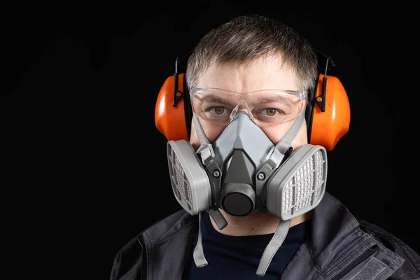 Portrait of a man wearing a respirator and protective noise-cancelling headphones earmuffs.