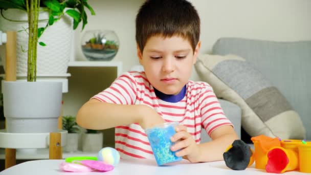 一个六岁的男孩坐在家里的桌子旁玩黏液游戏 儿童玩具一种用于培养儿童优秀运动技能和创造力的玩具 — 图库视频影像