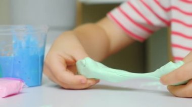 Altı yaşında bir çocuk evde bir masada otururken balçıkla oynuyor. Çocuklarda iyi motor beceriler ve yaratıcılık geliştirmek için bir oyuncak..
