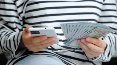 Yüz dolarlık banknotlar ve bir insanın elinde akıllı bir telefon.