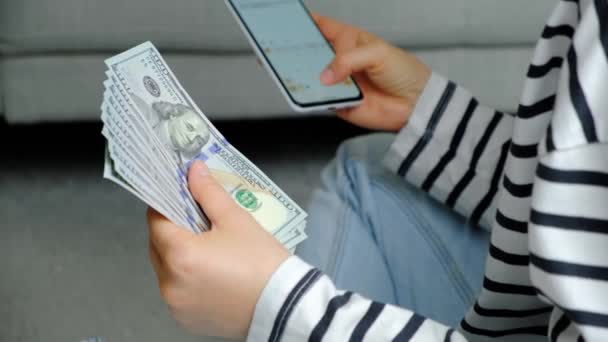 一个女人手里拿着许多100美元的钞票 在智能手机上用计算器计算利润 — 图库视频影像