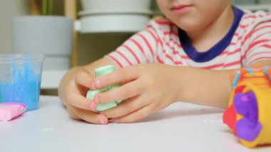 Altı yaşında bir çocuk evde bir masada otururken balçıkla oynuyor. Çocuklarda iyi motor beceriler ve yaratıcılık geliştirmek için bir oyuncak..
