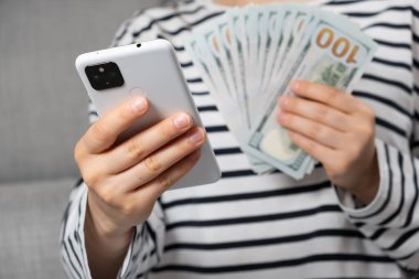 Yüz dolarlık banknotlar ve bir insanın elinde akıllı bir telefon.