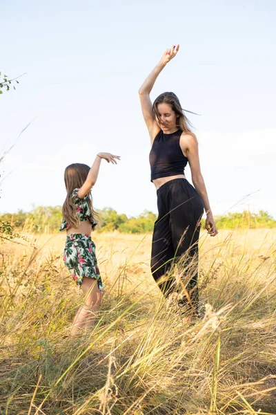 Mother and daughter have fun and dance in the summer field in nature. Mothers Day, happy motherhood and spending time together with the child.