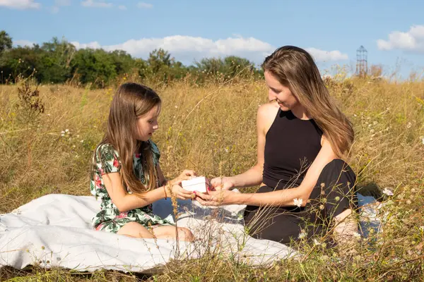 A five-year-old daughter gives a gift to her mother in nature in the summer field. Mothers Day, Happy Parenthood