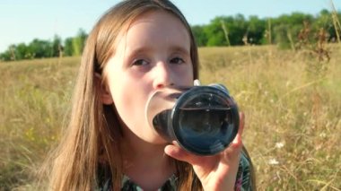 Küçük kız doğada cam bir şişeden su içiyor..