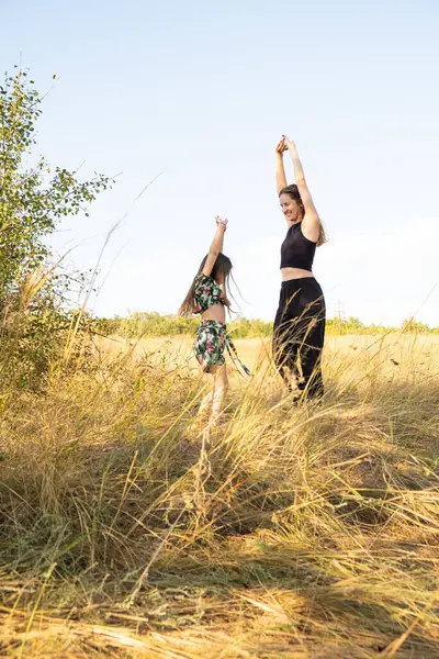 Mother and daughter have fun and dance in the summer field in nature. Mother\'s Day, happy motherhood and spending time together with the child.