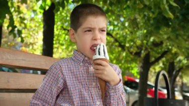 Küçük bir çocuk dışarıda bir bankta otururken dondurma yiyor.