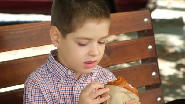 Băiețelul Mănâncă Burger Stând Bancă Aer Liber Mâncare Rapidă Stradă — Videoclip de stoc