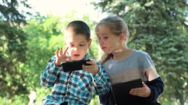 Çocuklar parkta otururken aletleri, akıllı telefon ve tablet oyunlarını kullanırlar..