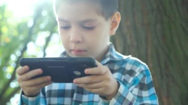 Yazın parkta otururken akıllı telefondan oyun oynayan küçük bir çocuk..