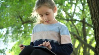 Küçük kız yazın parkta otururken bir tablet kullanır.