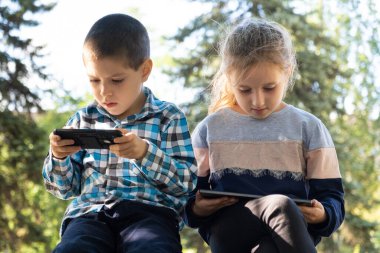 Çocuklar parkta otururken aletleri, akıllı telefon ve tablet oyunlarını kullanırlar..