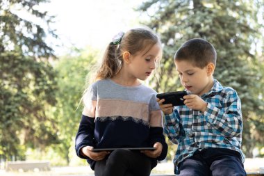 Çocuklar parkta otururken aletleri, akıllı telefon ve tablet oyunlarını kullanırlar..