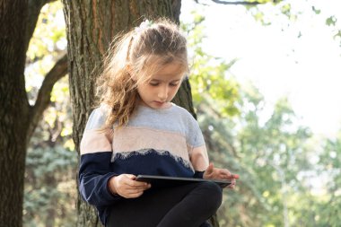 Küçük kız yazın parkta otururken bir tablet kullanır.