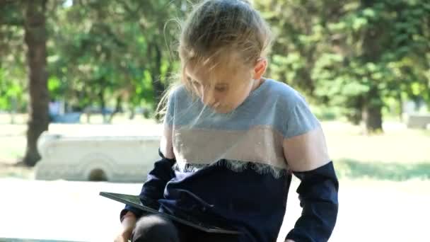 Küçük Kız Yazın Parkta Otururken Bir Tablet Kullanıyor Ekrana Bakıyor — Stok video