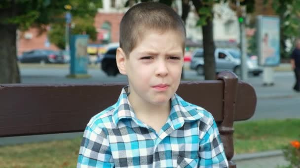 Mały Poważny Chłopiec Przeżuwa Coś Siedząc Ławce Ulicy Miasta Lecie — Wideo stockowe
