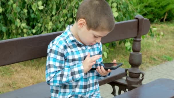 Malý Chlapec Používá Smartphone Zatímco Sedí Lavičce Parku Létě — Stock video