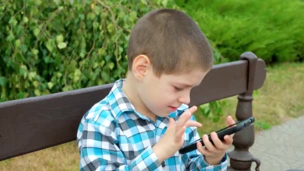 Маленький Мальчик Пользуется Смартфоном Сидя Летом Скамейке Парке — стоковое видео