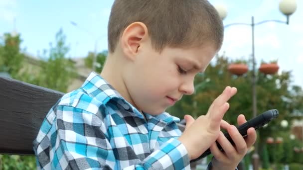 Маленький Хлопчик Використовує Смартфон Сидячи Лавці Парку Влітку — стокове відео