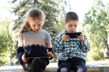 Çocuklar parkta otururken aletleri, akıllı telefon ve tablet oyunlarını kullanırlar..