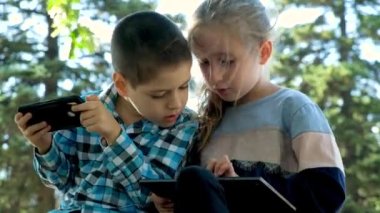 Çocuklar parkta otururken aletleri, akıllı telefon ve tablet oyunlarını kullanırlar..