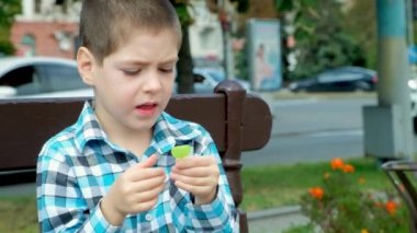 Küçük bir çocuk şehirde bir bankta otururken lolipop yiyor..